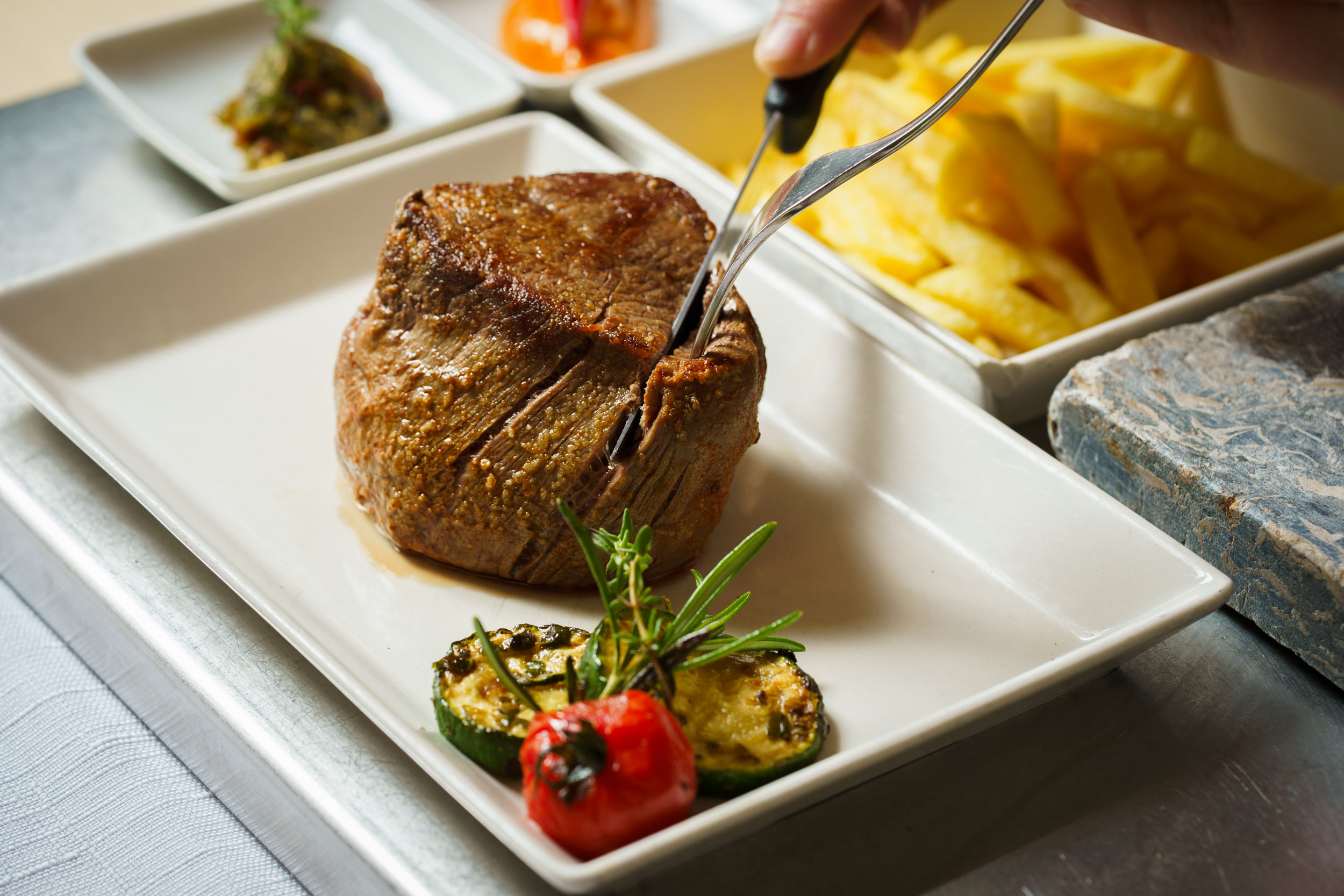 Restaurant: Beef fillet with vegetables being carved for roasting on the hot stone at the table