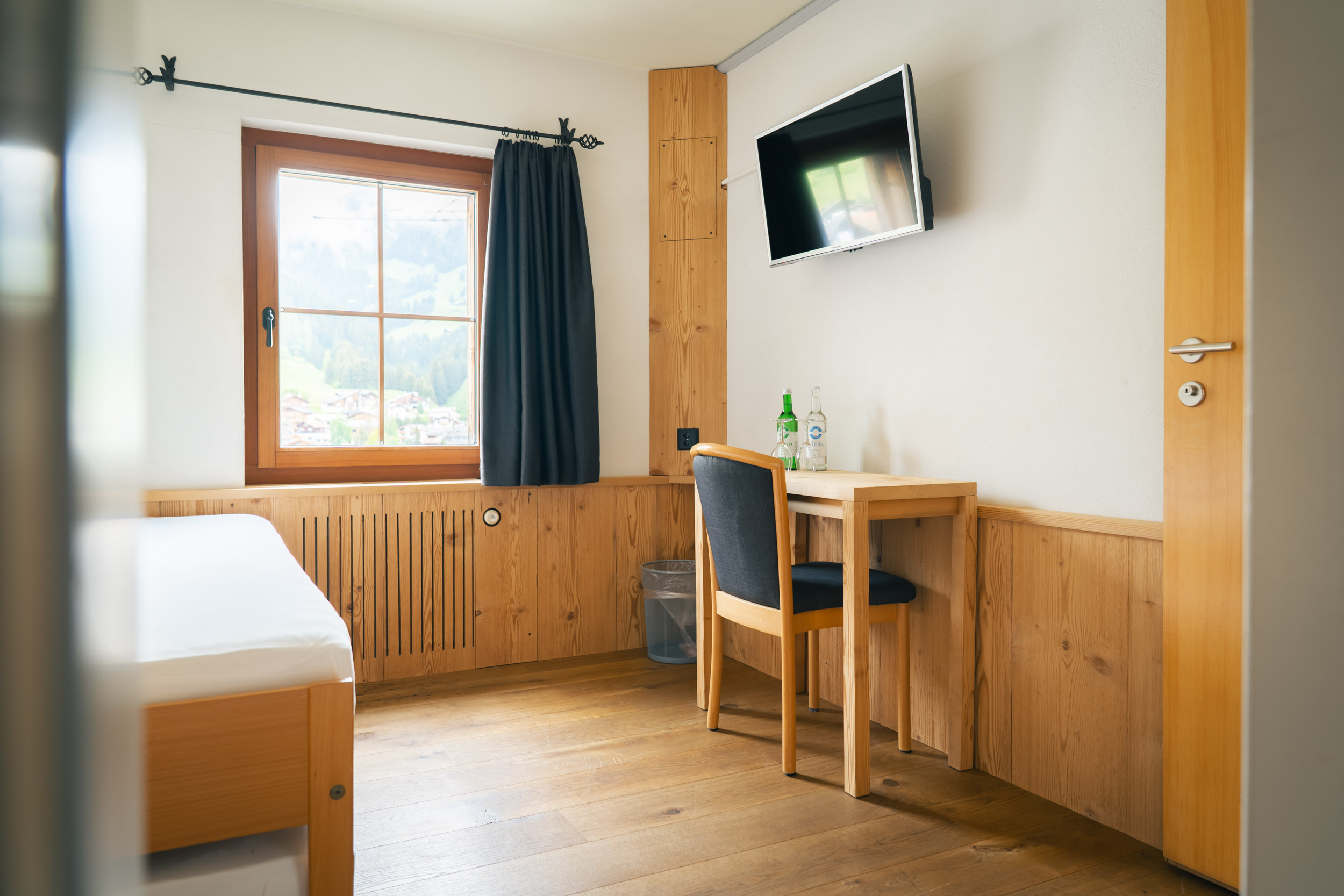Single room with a single bed, desk, and TV with parquet flooring
