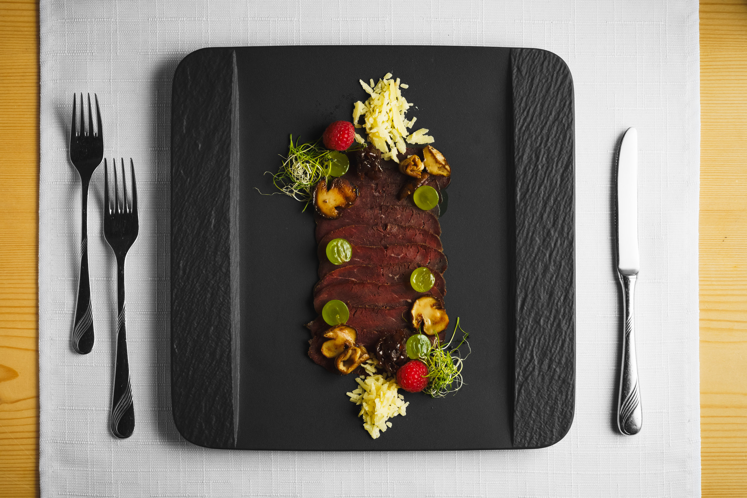 Dish: Venison carpaccio "Alpina style," served on a black plate, beautifully garnished – Brigels