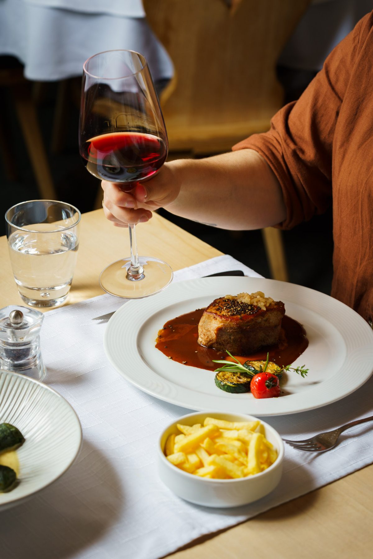 Restaurant: Toasting with red wine, accompanied by a pepper steak with French fries